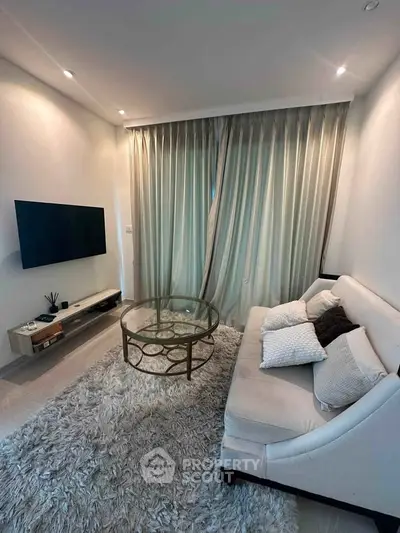 Modern living room with elegant decor, featuring a plush sofa, glass coffee table, and wall-mounted TV.
