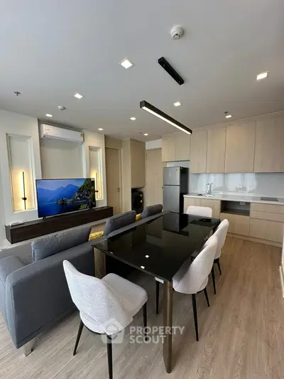 Modern open-plan living room with sleek kitchen and dining area, featuring stylish furniture and appliances.