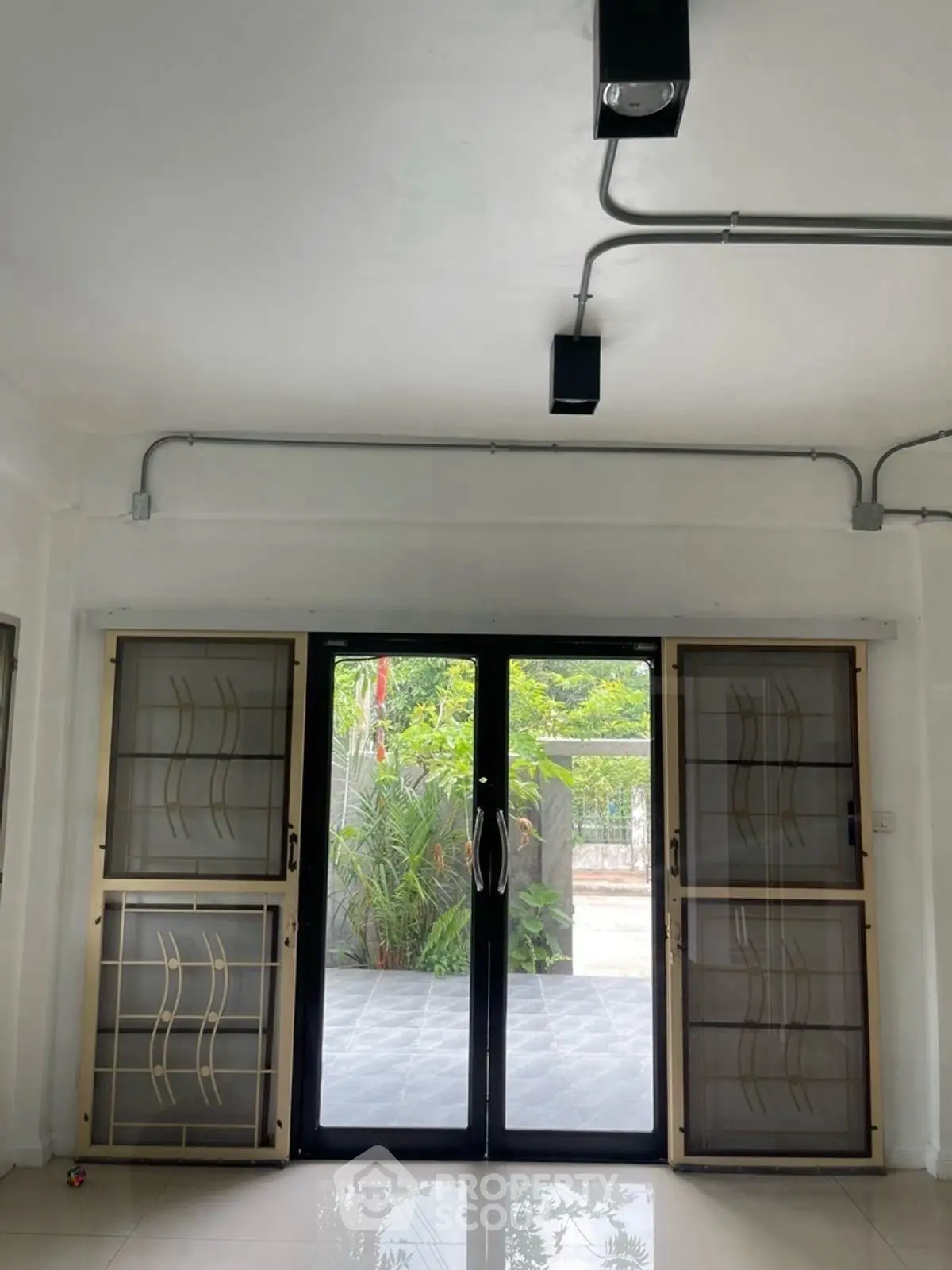 Modern interior with glass doors opening to a lush garden view, featuring sleek metal accents and tiled flooring.