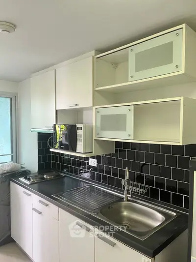 Modern kitchen with sleek black tile backsplash and white cabinetry, featuring a stainless steel sink and microwave.