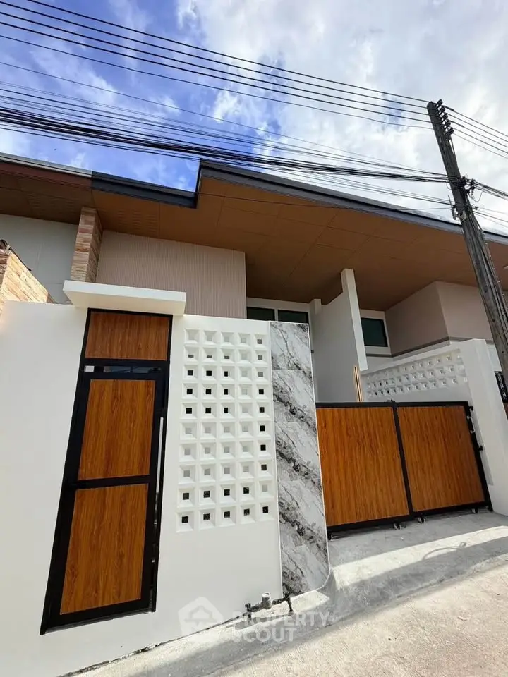 Modern house exterior with stylish wooden gate and marble accents under a clear blue sky.
