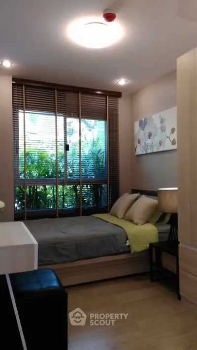 Cozy bedroom with modern decor and large window overlooking lush greenery.