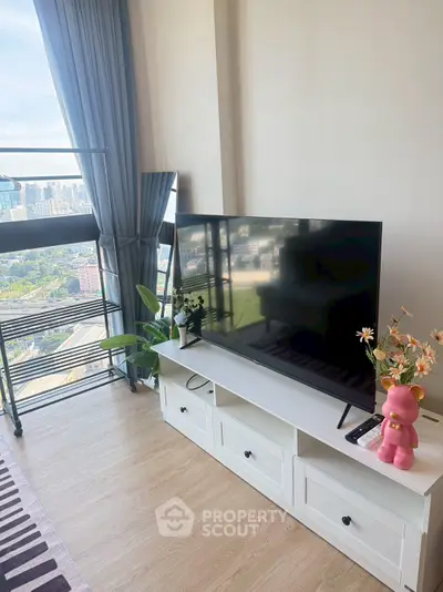 Modern living room with large TV and city view, featuring stylish decor and floor-to-ceiling windows.