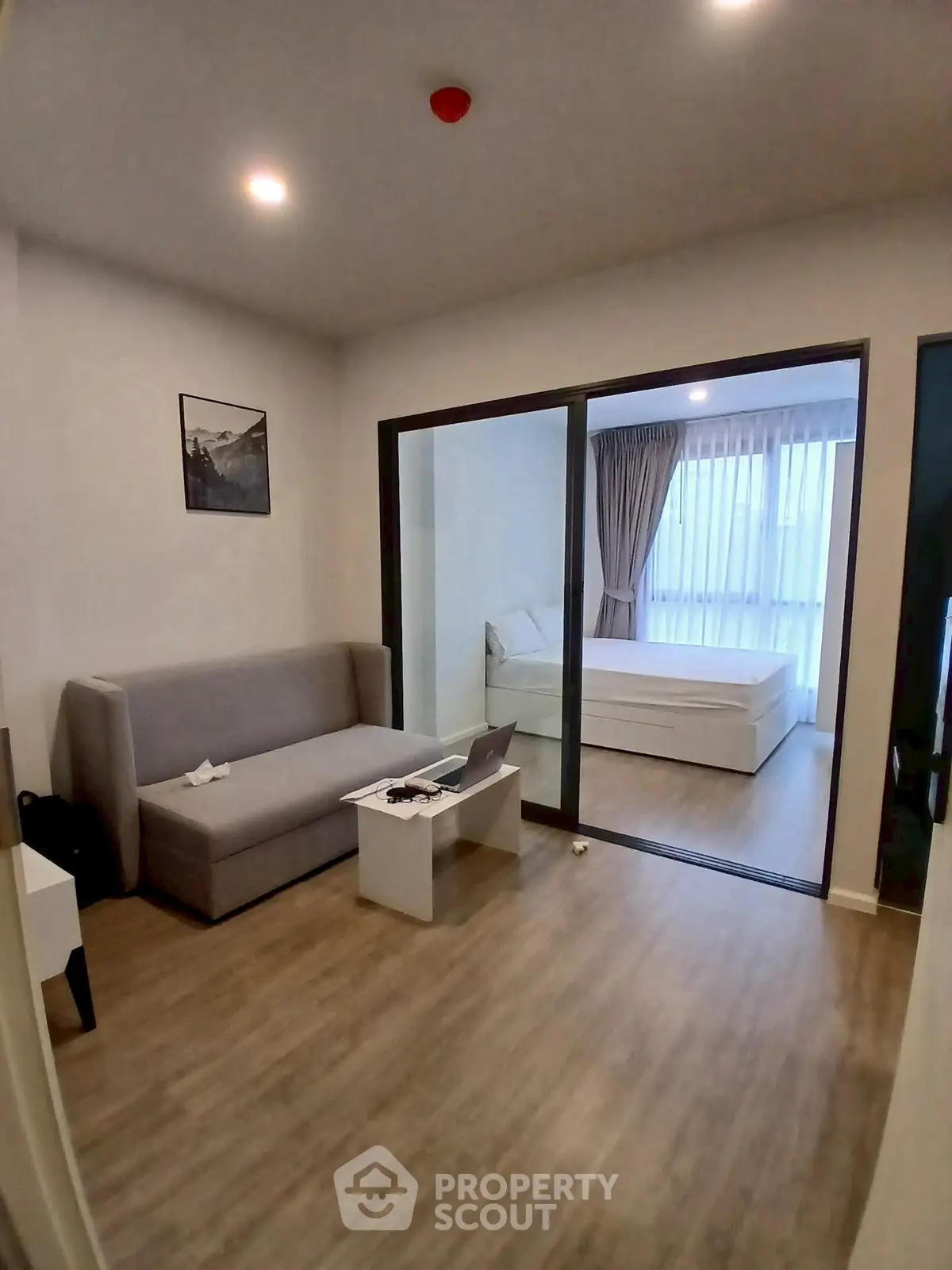 Modern living room with sliding glass doors leading to a cozy bedroom, featuring stylish decor and ample natural light.