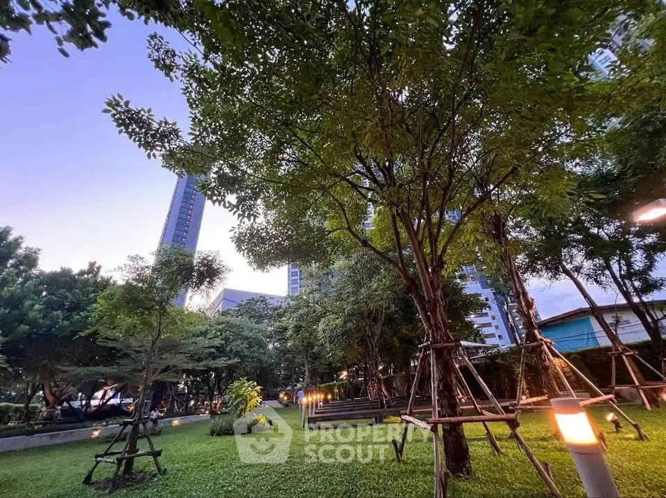 Lush green garden with tall trees and modern buildings in the background, perfect for relaxation.