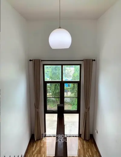 Spacious interior with large window and elegant lighting, offering a serene view of greenery.