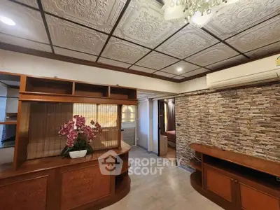 Charming living room with elegant ceiling tiles and stone accent wall, featuring built-in wooden cabinetry and air conditioning.