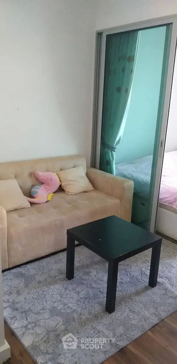 Cozy small living room with beige sofa and black coffee table, adjacent to a bedroom with sliding glass door.