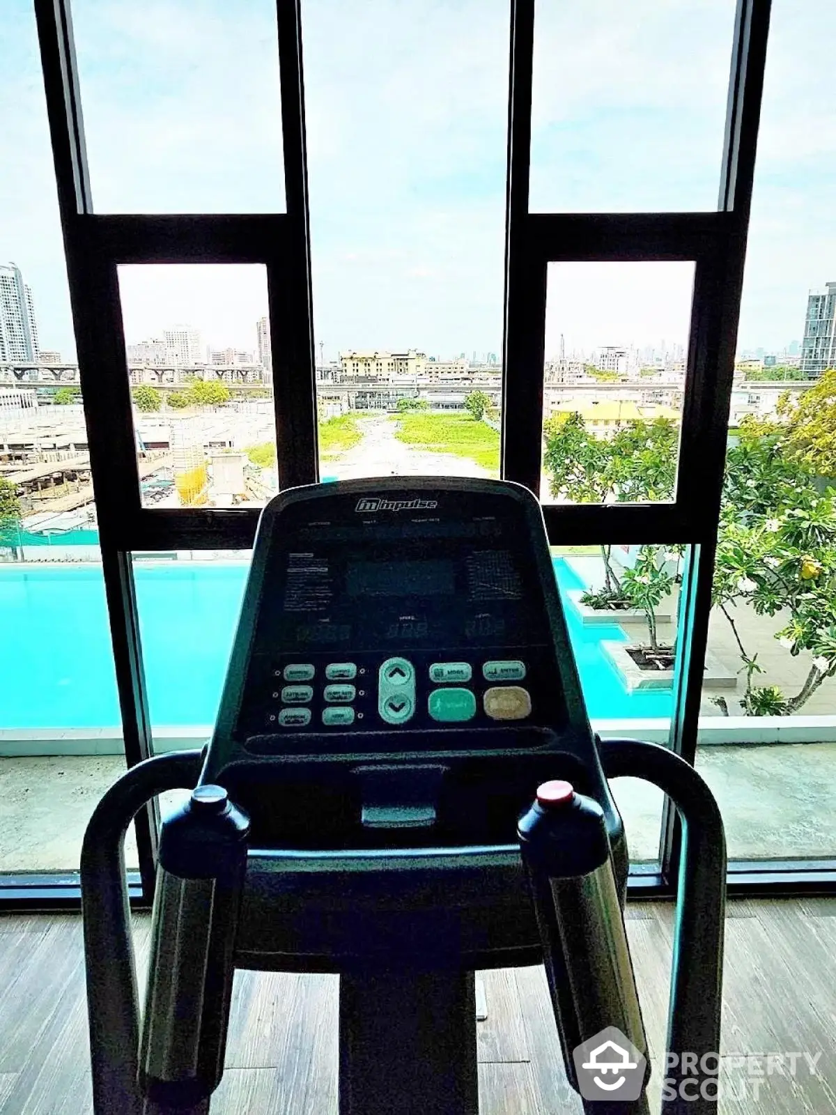 Modern gym with city view and pool, featuring exercise equipment and large windows.