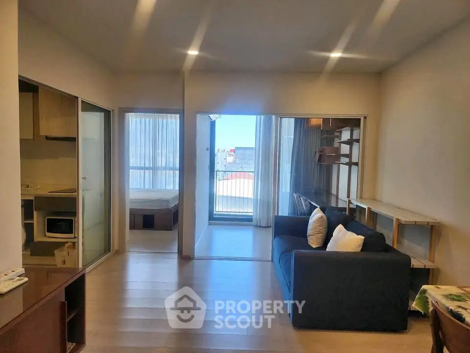 Modern living room with open layout and balcony view, featuring sleek furniture and natural light.