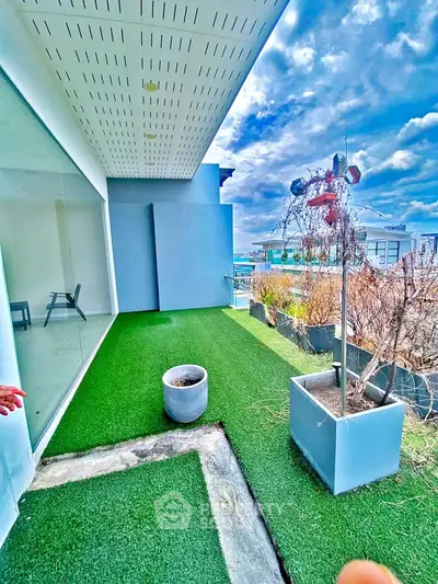 Spacious balcony with artificial grass and modern planters offering a serene outdoor retreat with city views.