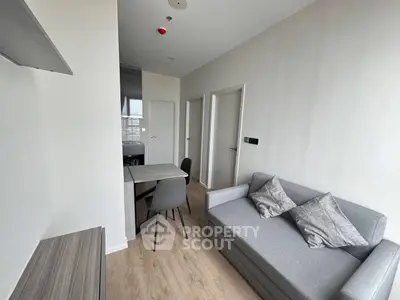 Modern living room with cozy gray sofa and dining area in a compact apartment.