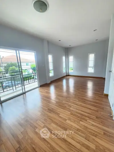 Spacious empty room with wooden flooring and balcony access in modern home