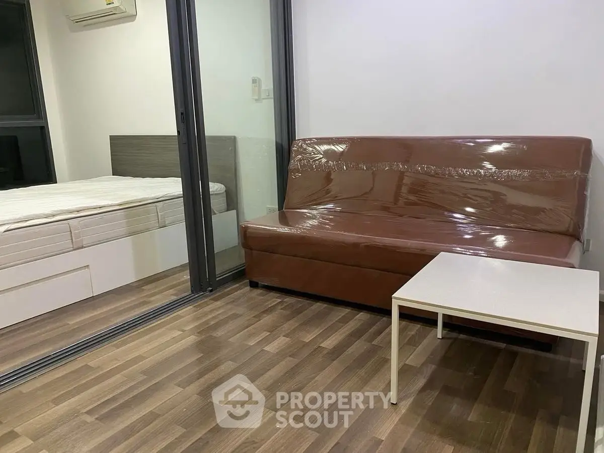 Modern studio apartment with glass partition, brown sofa, and wooden flooring.