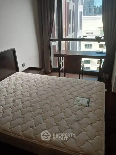 Cozy bedroom with large window and city view, featuring a comfortable bed and a study desk.