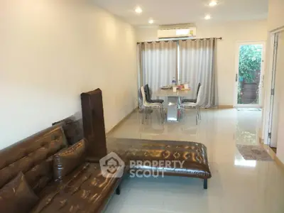 Spacious living room with glossy tiled flooring, large brown sofa, and an elegant dining area leading to a cozy garden view.