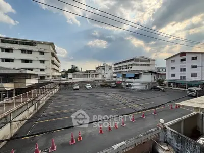 Spacious urban parking lot with surrounding buildings under a partly cloudy sky, ideal for commercial use.