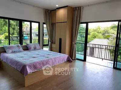 Spacious bedroom with large windows and balcony offering lush green views.