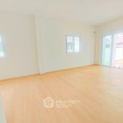 Spacious empty room with light wood flooring and large windows for natural light.