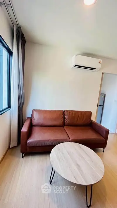 Modern living room with brown leather sofa and air conditioning, featuring a sleek coffee table and natural light.