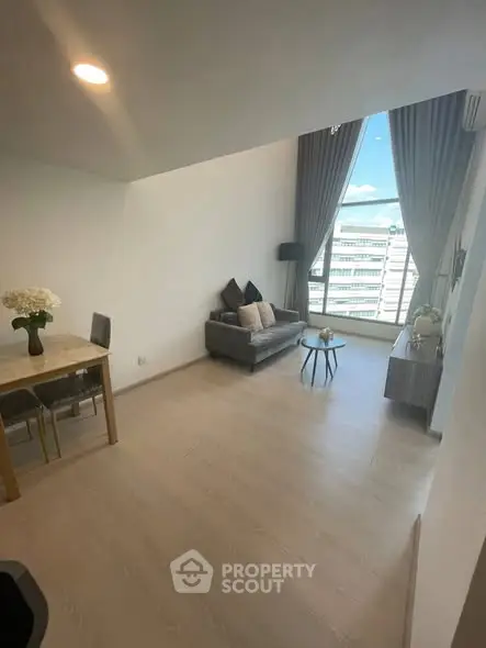 Spacious modern living room with high ceiling and large window offering city view.