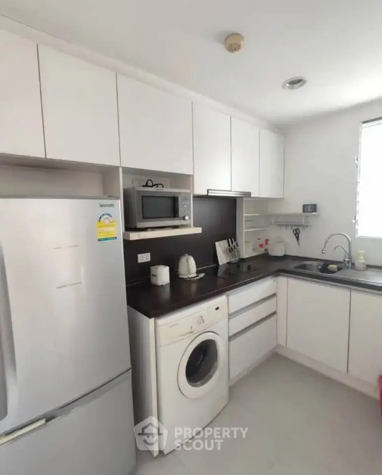 Modern kitchen with sleek white cabinets, washing machine, and stainless steel appliances.