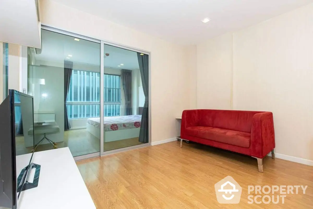 Modern living room with red sofa and glass partition leading to bedroom