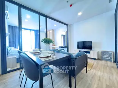 Modern open-plan living room with dining area and glass partition, featuring stylish decor and natural light.