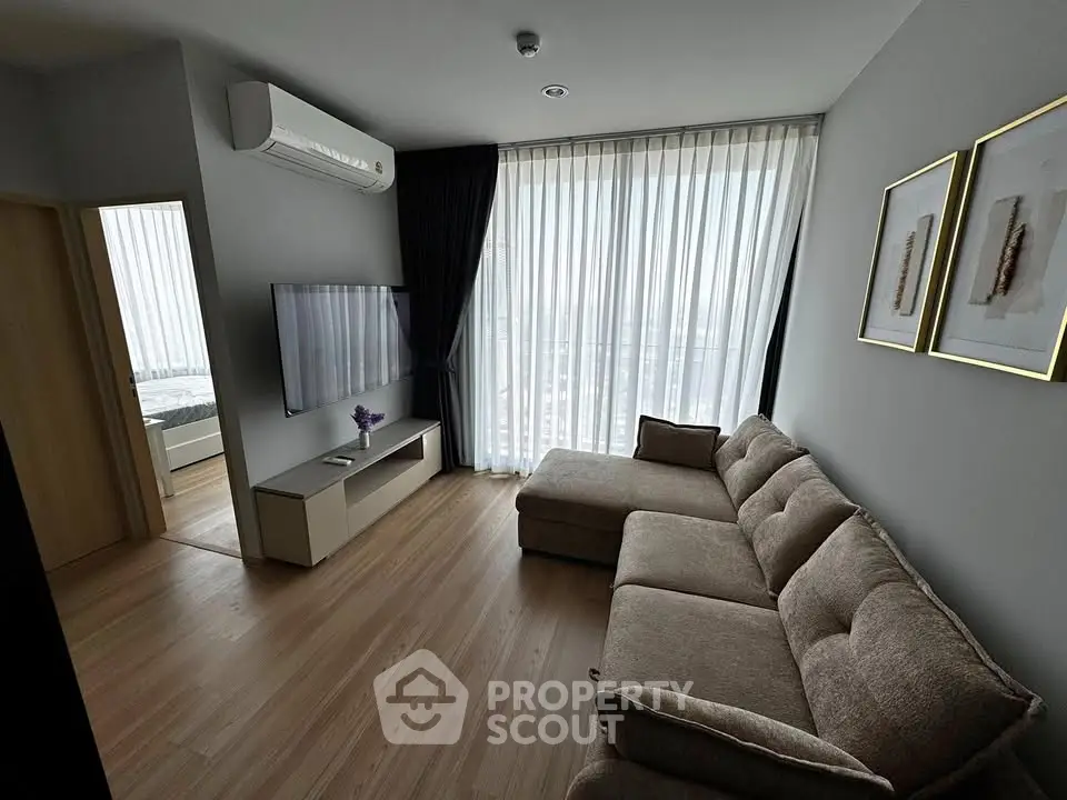 Modern living room with large window, cozy sectional sofa, and wall-mounted TV in a stylish apartment.
