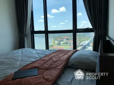 Spacious bedroom with large windows offering a panoramic view of the cityscape and waterfront, bathed in natural light.