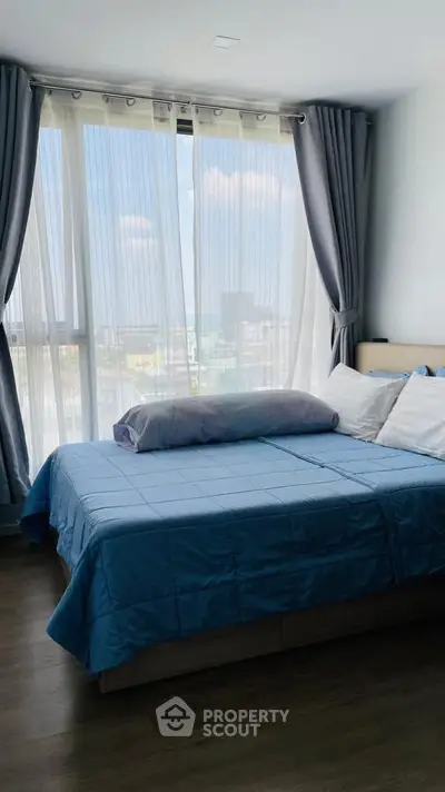 Bright and cozy bedroom with large window and blue bedding, offering a serene city view.