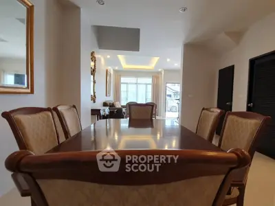 Elegant dining area with wooden table and chairs, leading to a cozy living room with modern lighting.