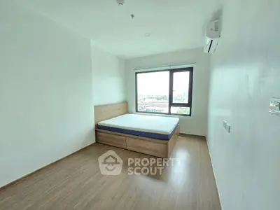 Spacious bedroom with wooden flooring and large window offering city views.