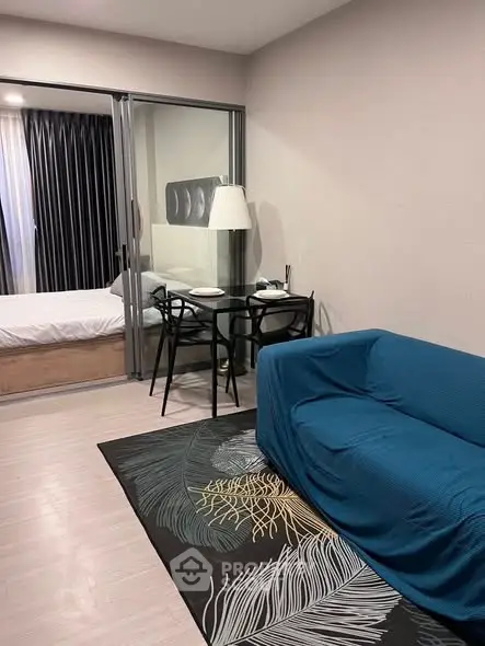 Modern living room with blue sofa and glass partition leading to bedroom