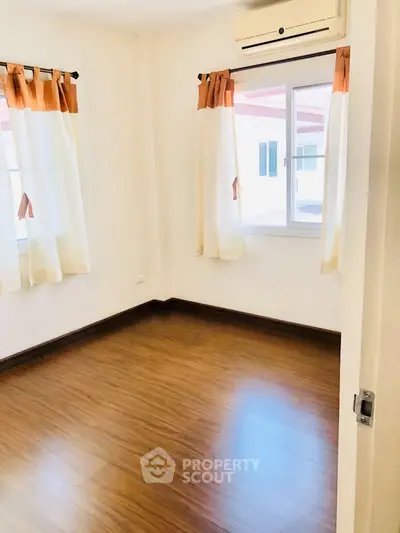 Bright and airy bedroom with wooden flooring and large windows in a modern apartment.