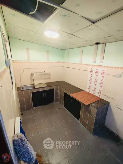 Compact kitchen with tiled flooring and basic cabinetry, ideal for renovation.