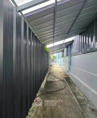 Narrow outdoor corridor with metal roofing and siding, ideal for utility access.