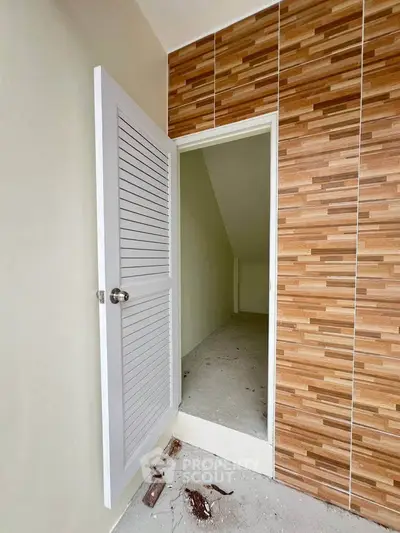 Compact storage room with wooden accent wall and white door, ideal for organizing essentials.