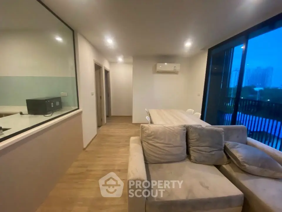 Modern living room with cozy sofa and dining area, featuring large windows and wooden flooring.