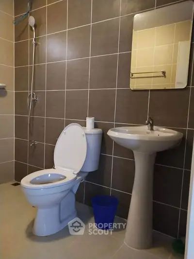 Modern bathroom with sleek pedestal sink and wall-mounted shower in tiled setting.