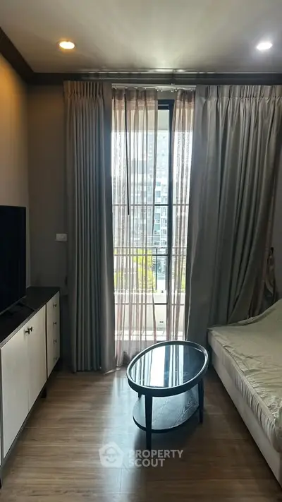 Cozy bedroom with modern decor, featuring a large window with city view and elegant curtains.