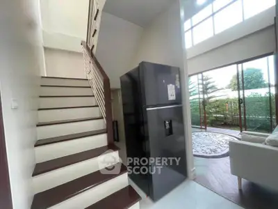 Modern home interior with staircase, sleek black fridge, and bright living area with garden view.