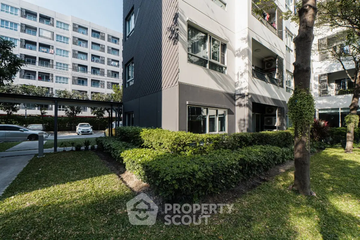 Modern apartment building exterior with lush green landscaping and parking area.