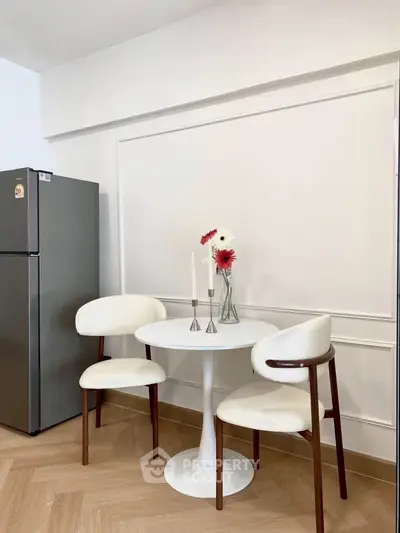 Chic dining nook with modern table, elegant chairs, and sleek fridge in stylish apartment.