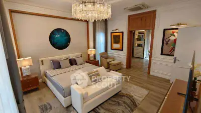 Luxurious bedroom with elegant decor, featuring a plush bed, stylish chandelier, and modern artwork.