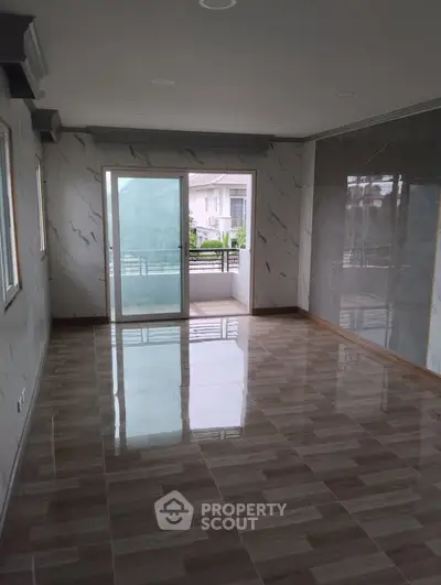 Spacious living room with marble walls and glossy tiled floor, leading to a balcony with a view.