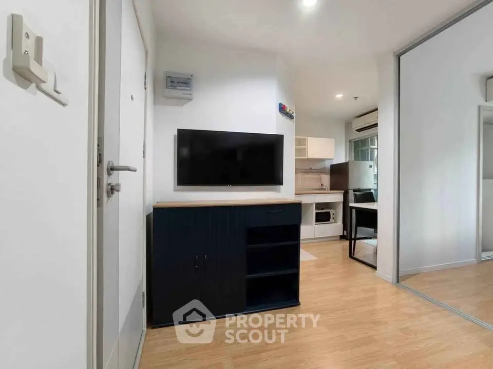Modern apartment interior with sleek kitchen and cozy living area, featuring a wall-mounted TV and stylish wooden flooring.