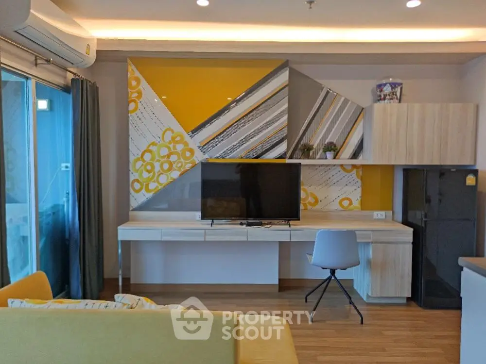 Modern living room with stylish decor and large TV, featuring a bright yellow accent wall and sleek furniture.