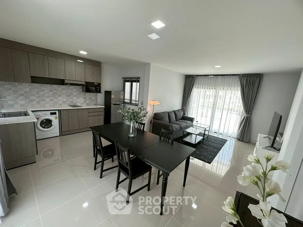 Modern open-plan living room with sleek kitchen and dining area, featuring stylish furniture and natural light.