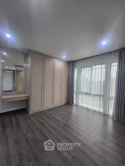 Spacious bedroom with elegant wood flooring and large windows for natural light.